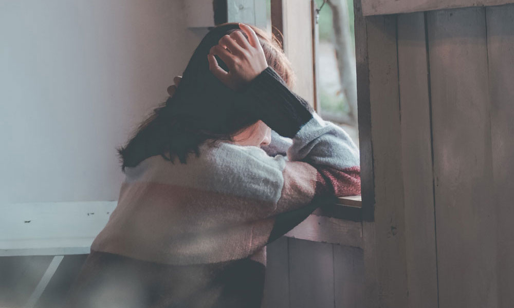 Someone looking out of a window with their head in thier hands, despairing